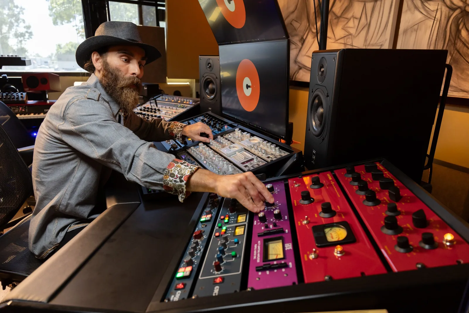 Photo of an engineer seated at an analog mastering desk with rack-mounted hardware units, viewed from the side in a studio environment.
